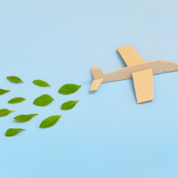 Wooden airplane model emitting fresh green leaves on blue background. Sustainable travel; clean and green energy; and biofuel for aviation industry concept.